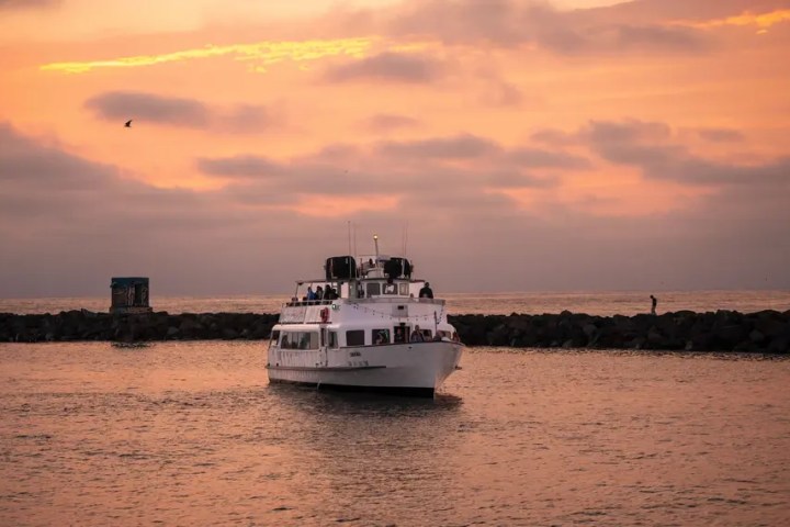 Boat approaching a rocky shore under a pink-orange sunset sky.