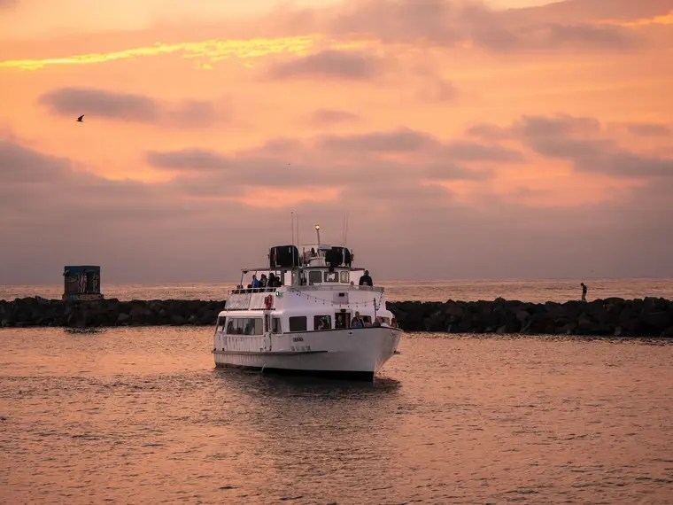 Boat approaching a rocky shore under a pink-orange sunset sky.