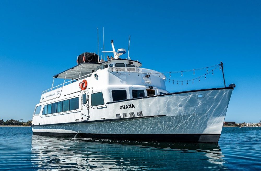 White boat named Ohana on calm water under clear blue sky.