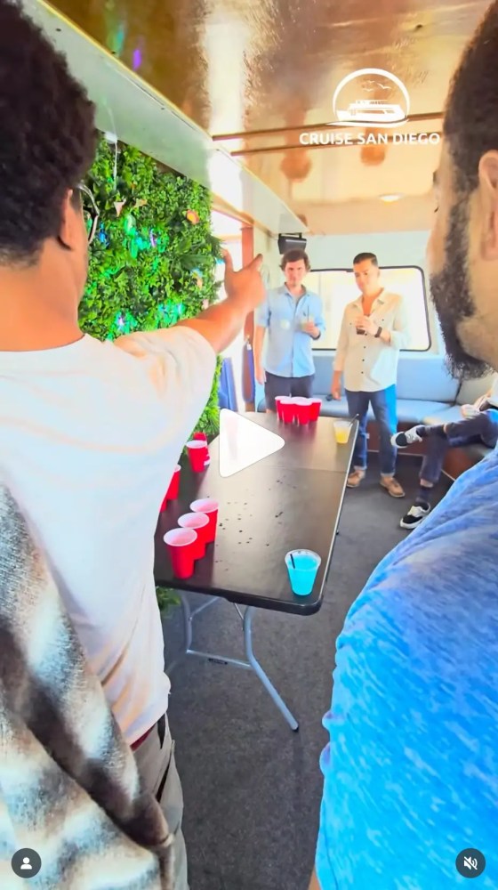 People playing beer pong on a boat with red cups on a table.