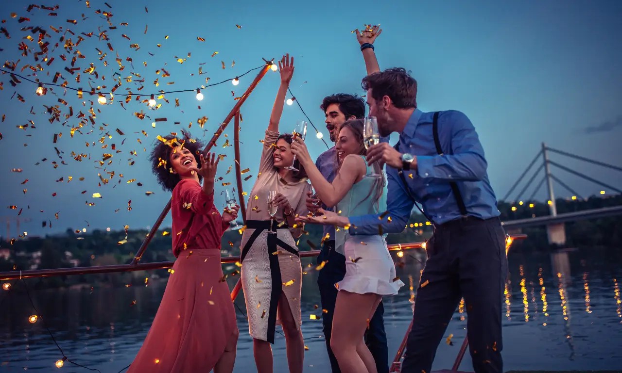 Corporate Event Cruise San Diego Group of friends celebrating outdoors at dusk with confetti and string lights.