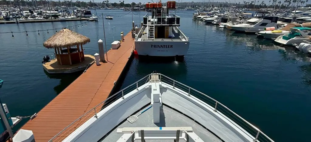 View from boat deck approaching a dock with a thatched hut and boats in the harbor.
