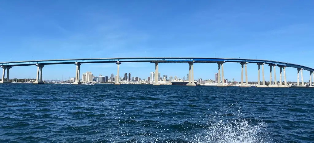 A long bridge over a wide body of water with a city skyline in the background under a clear blue sky.
