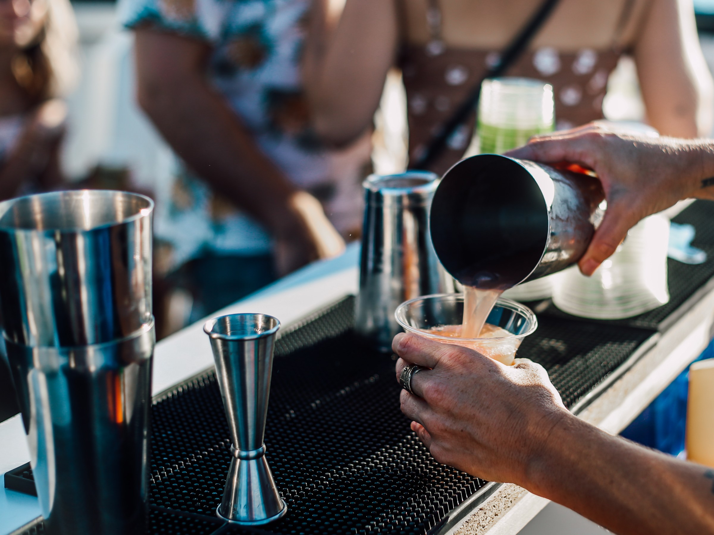 Bartender pouring a drink into a plastic cup at an outdoor bar.
