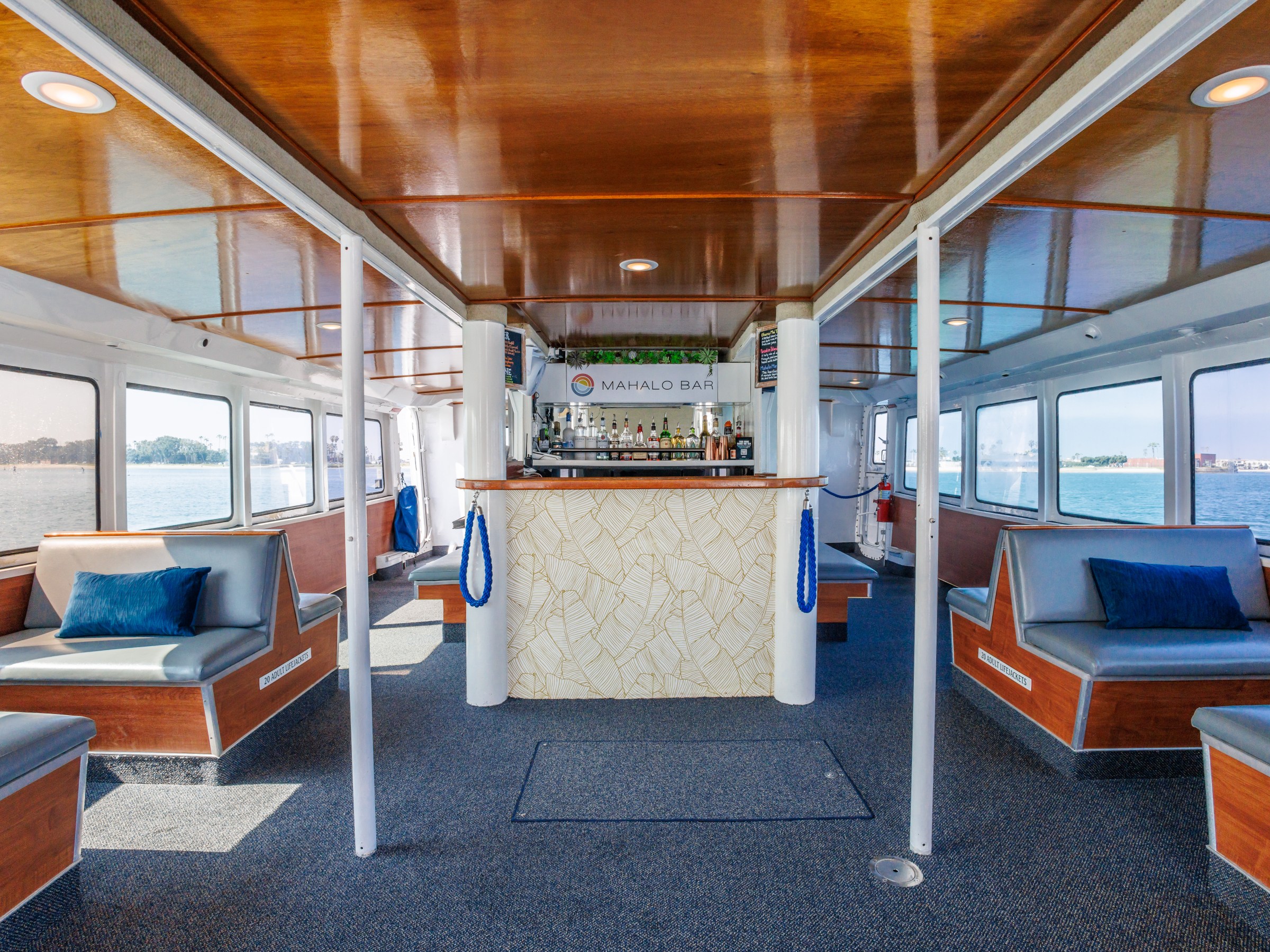 Interior of a boat with a bar and seating, featuring large windows and wooden ceiling.