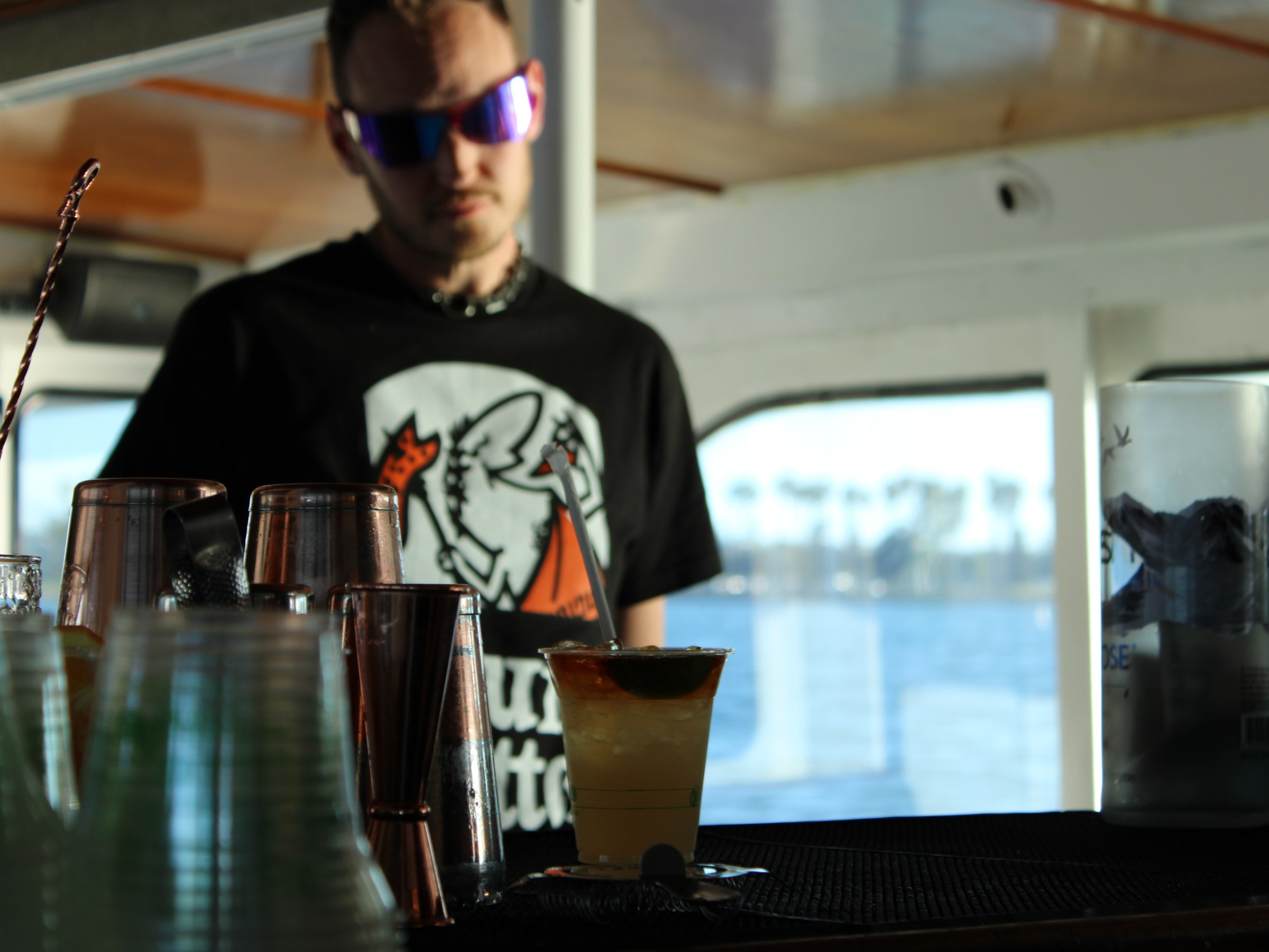 Person with sunglasses behind a bar counter with drinks.