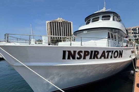 White boat named Inspiration docked near city buildings under clear sky.