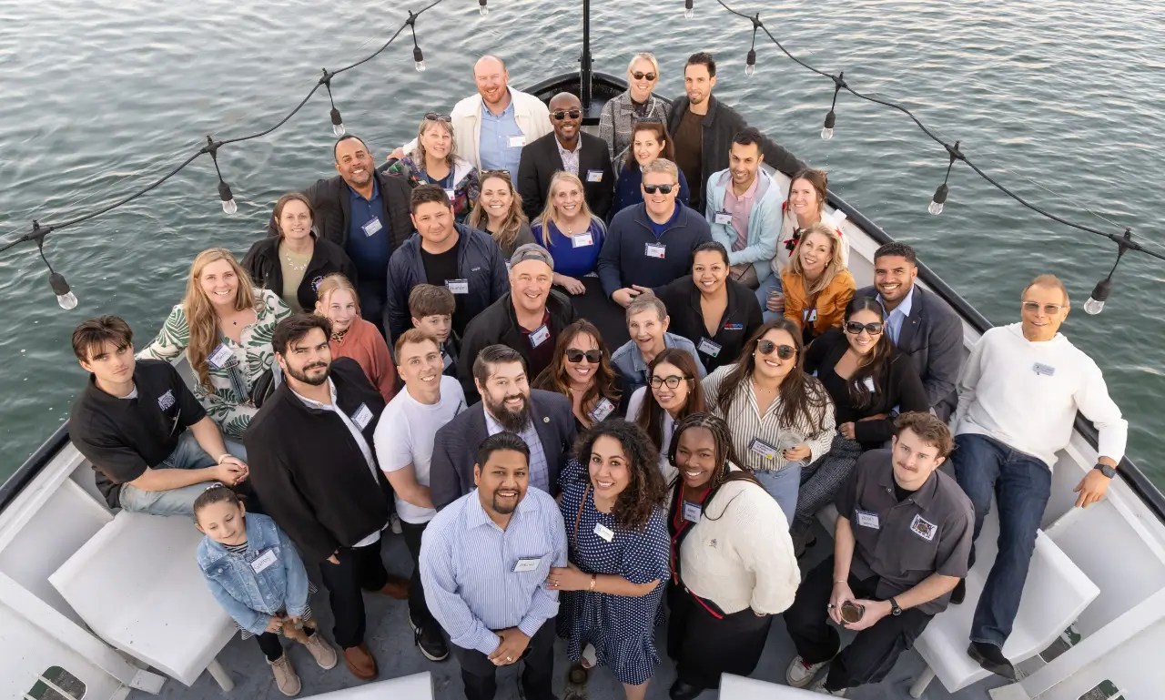 Group of people posing on a boat deck, with festive lights above.